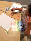 Young child placing stickers on a craft project alongside colorful shape stickers, Prang watercolors, and the book Ish — hands-on fine motor activity from a Rooted in Writing subscription box.
